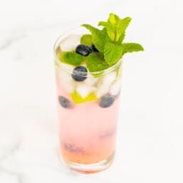 A fresh blueberry mojito garnished with mint, lime and blueberries on a marble surface.