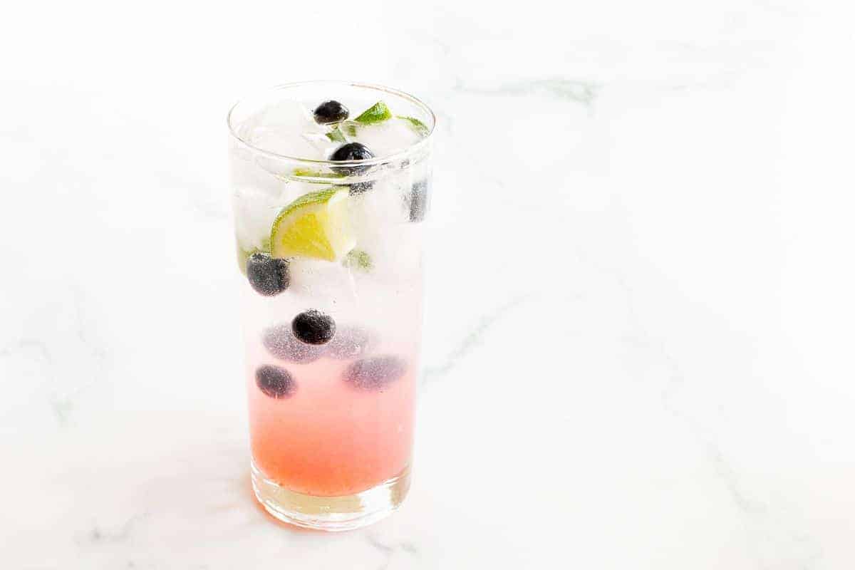 A clear glass with a blueberry mojito cocktail before mixing.