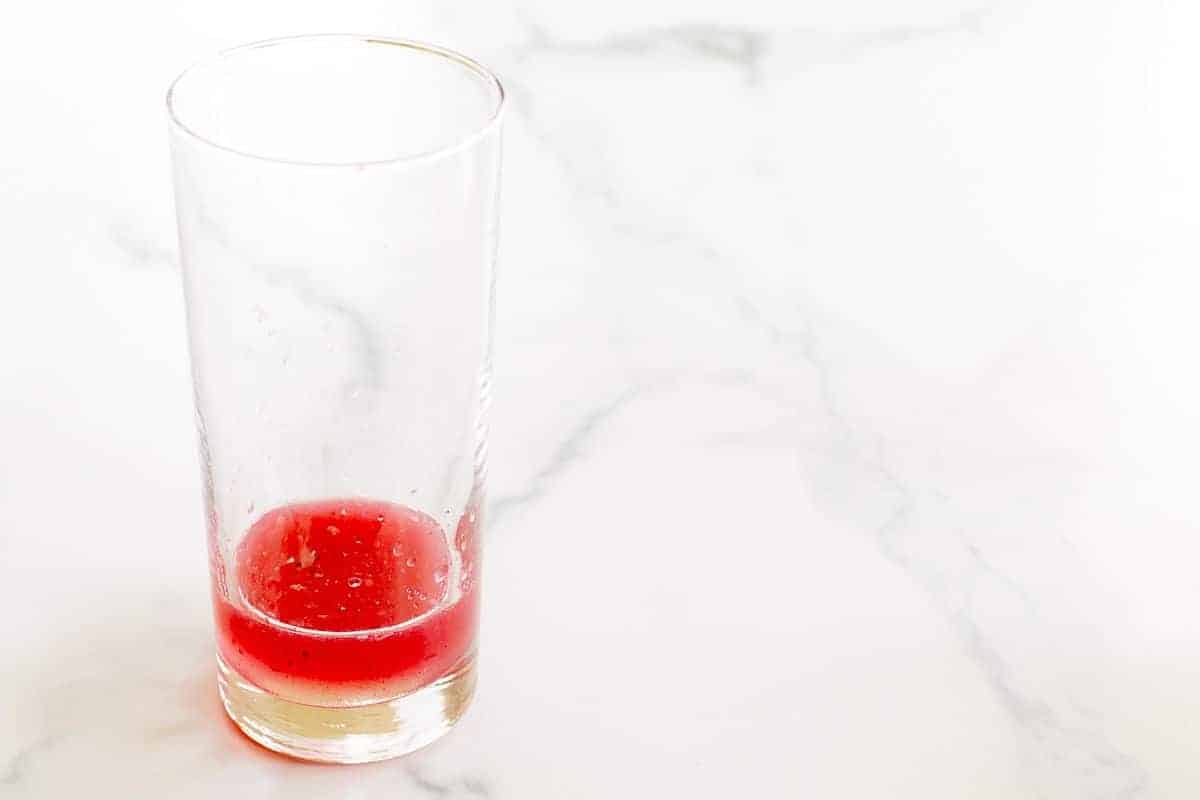A clear glass on a marble surface, filled with a little pink liquid at the bottom.