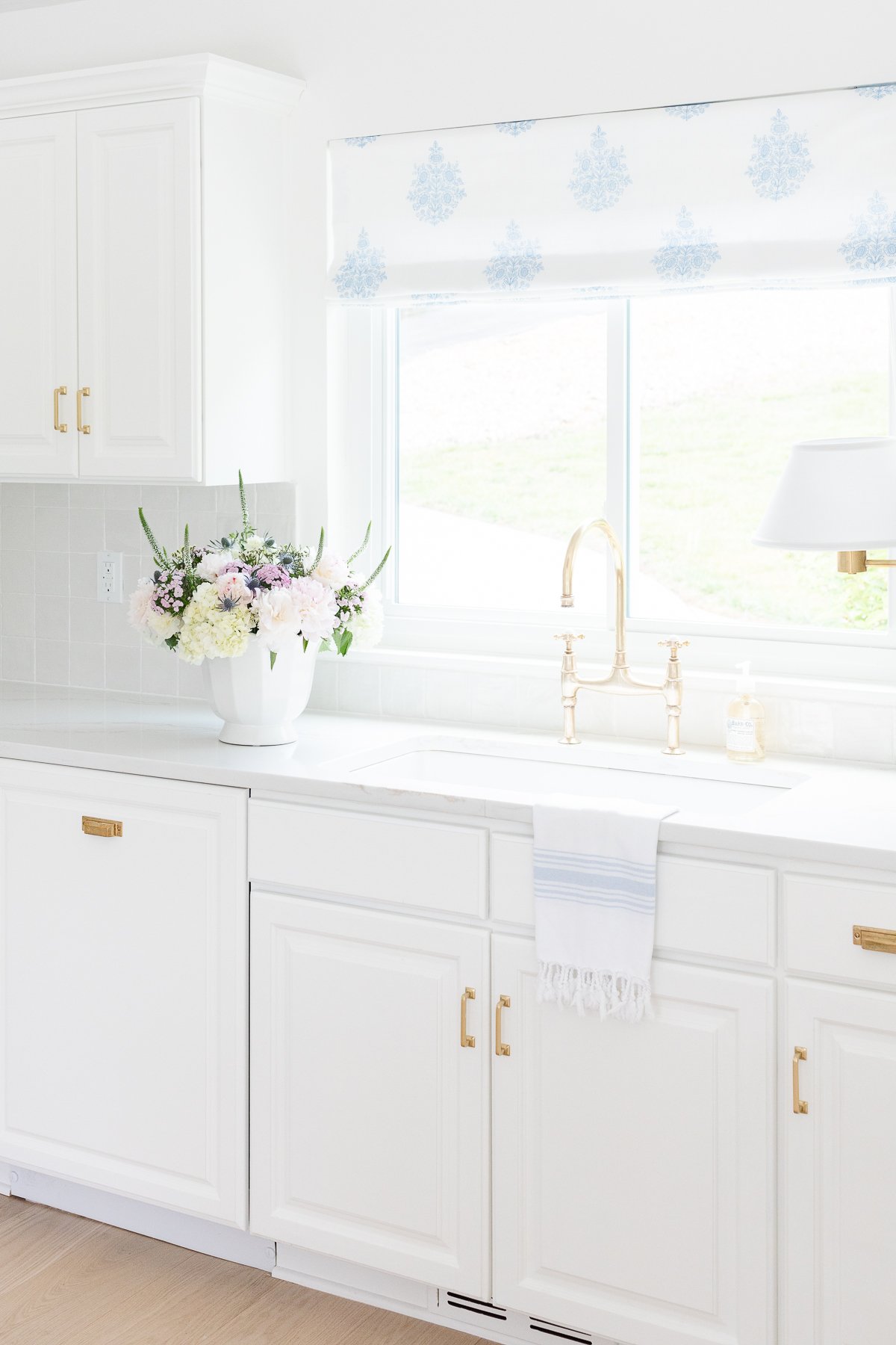 A white kitchen with a brass bridge faucet over the sink.