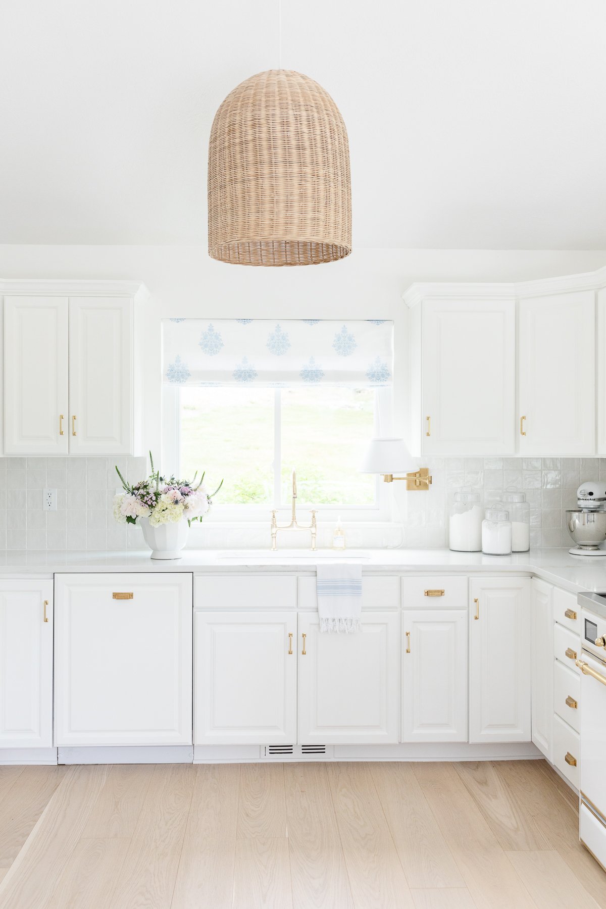 A white kitchen with a brass bridge faucet over the sink.