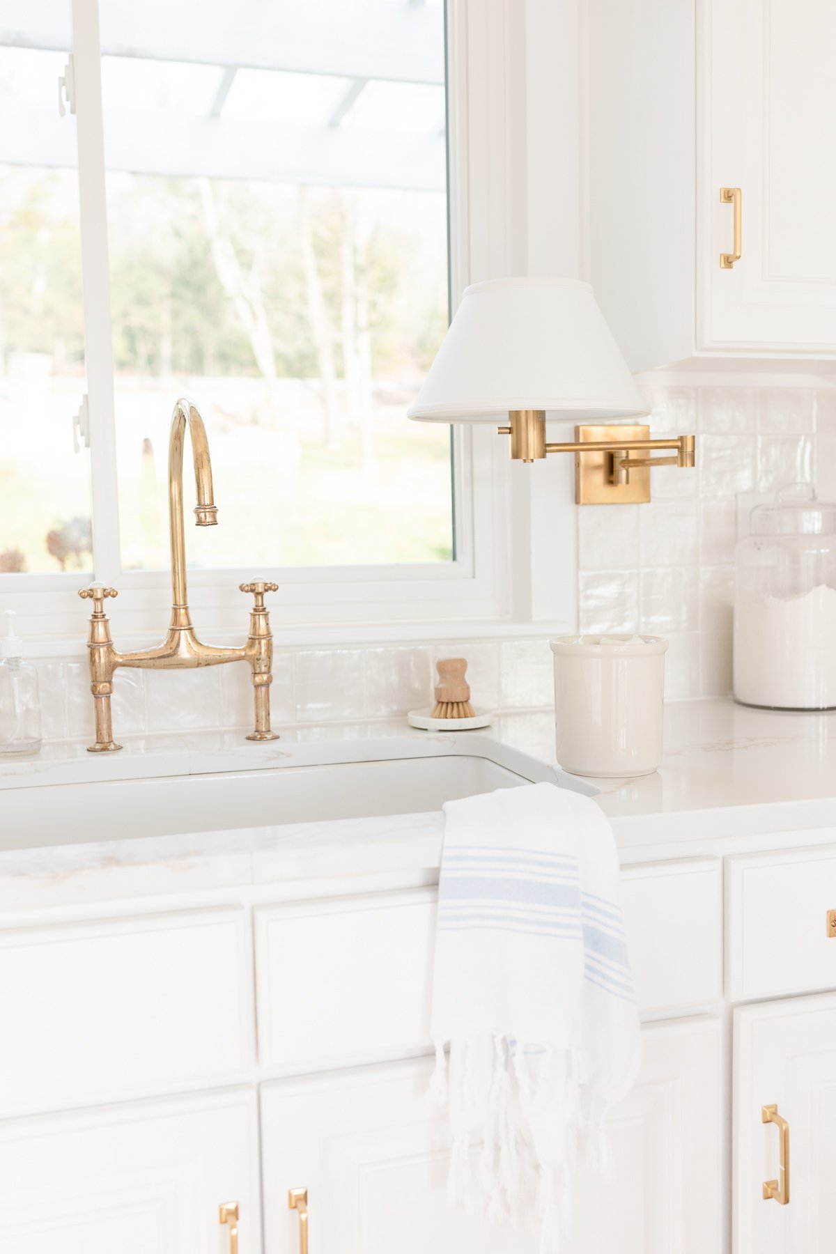 A white kitchen with a brass bridge faucet over the sink.