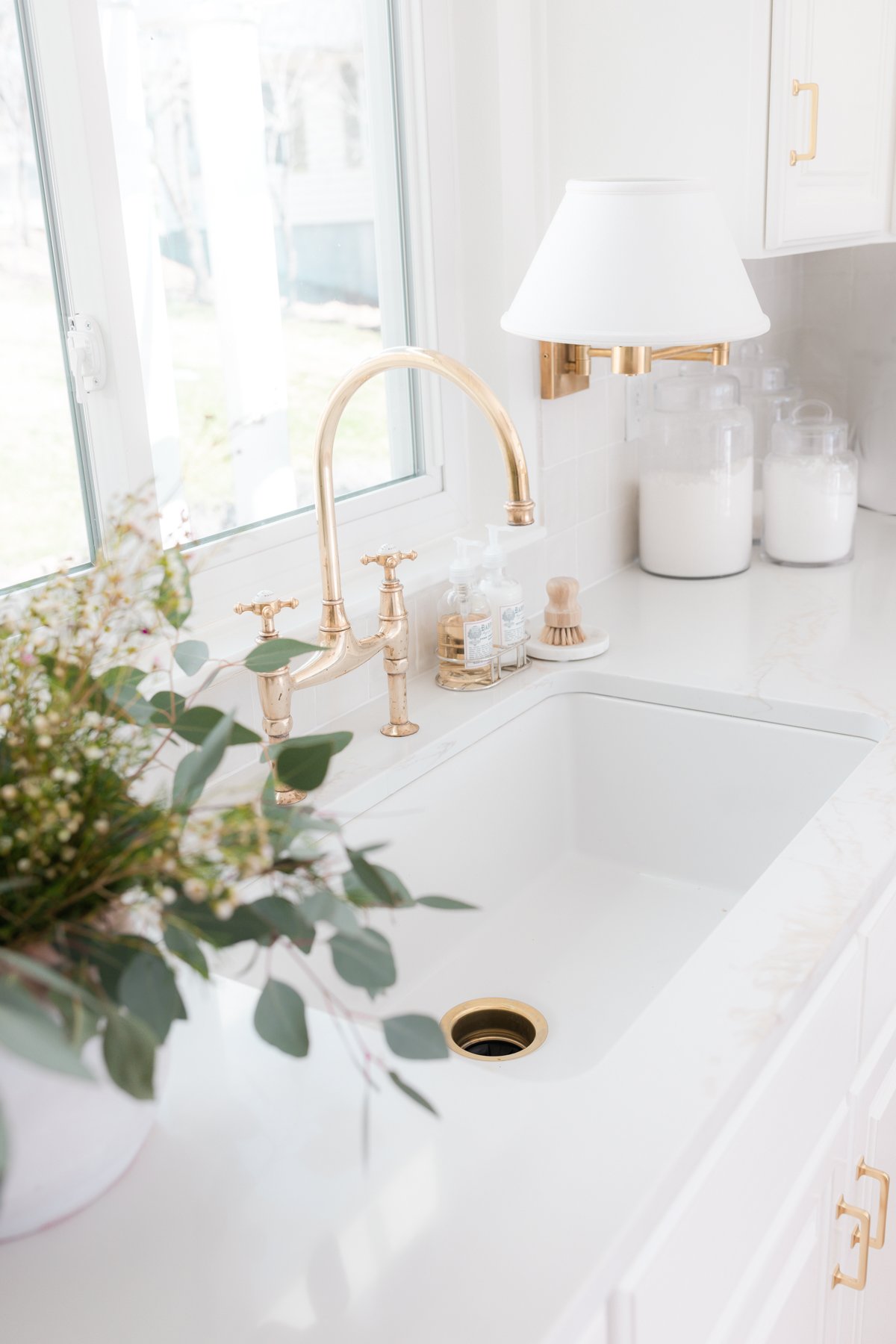 A white kitchen with a brass bridge kitchen faucet over the sink.