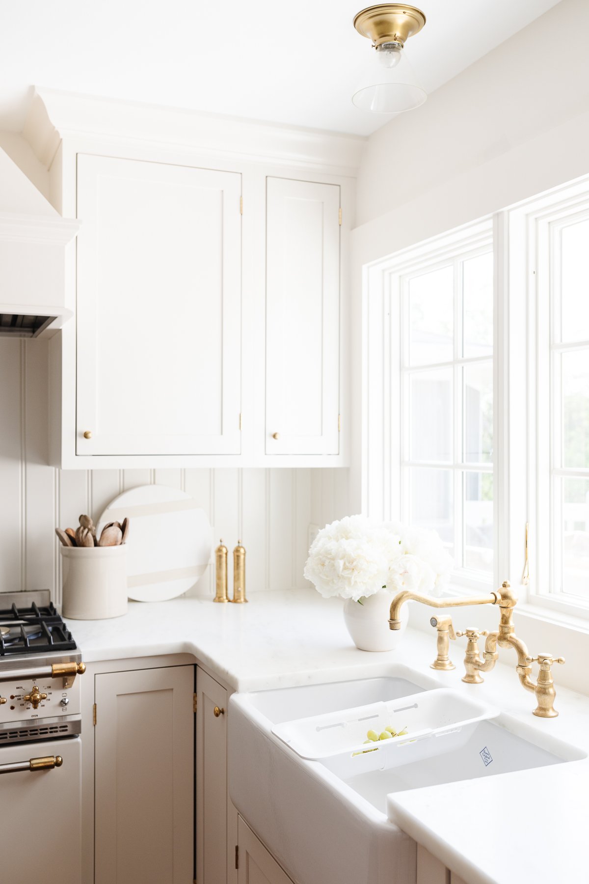 An unlacquered brass bridge kitchen faucet over a white farmhouse sink.