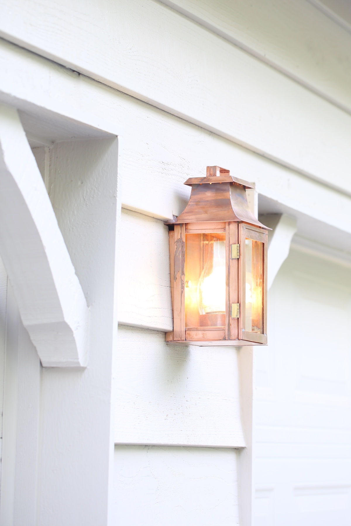 A copper lantern on the white painted exterior of a home.