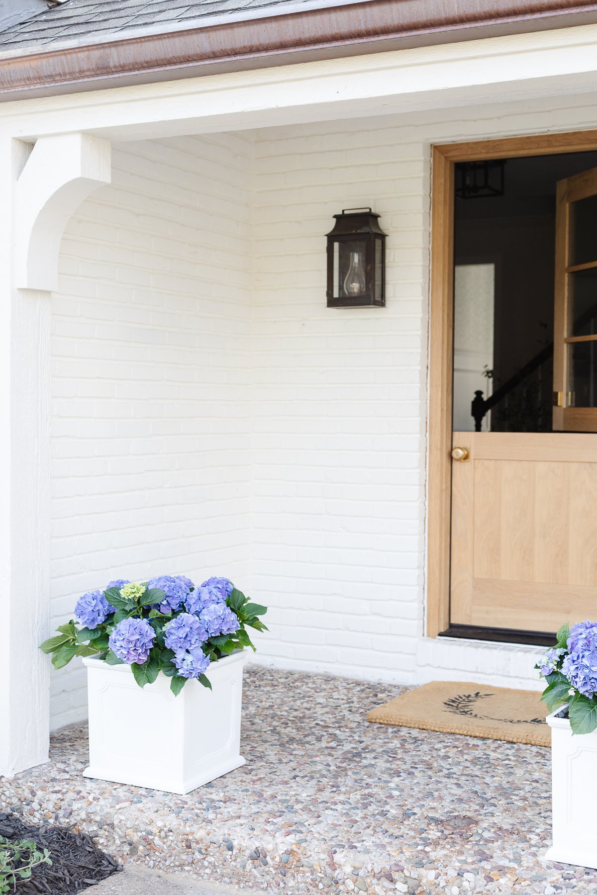 An entryway to a white brick home with copper lanterns on either side of the wooden Dutch door.