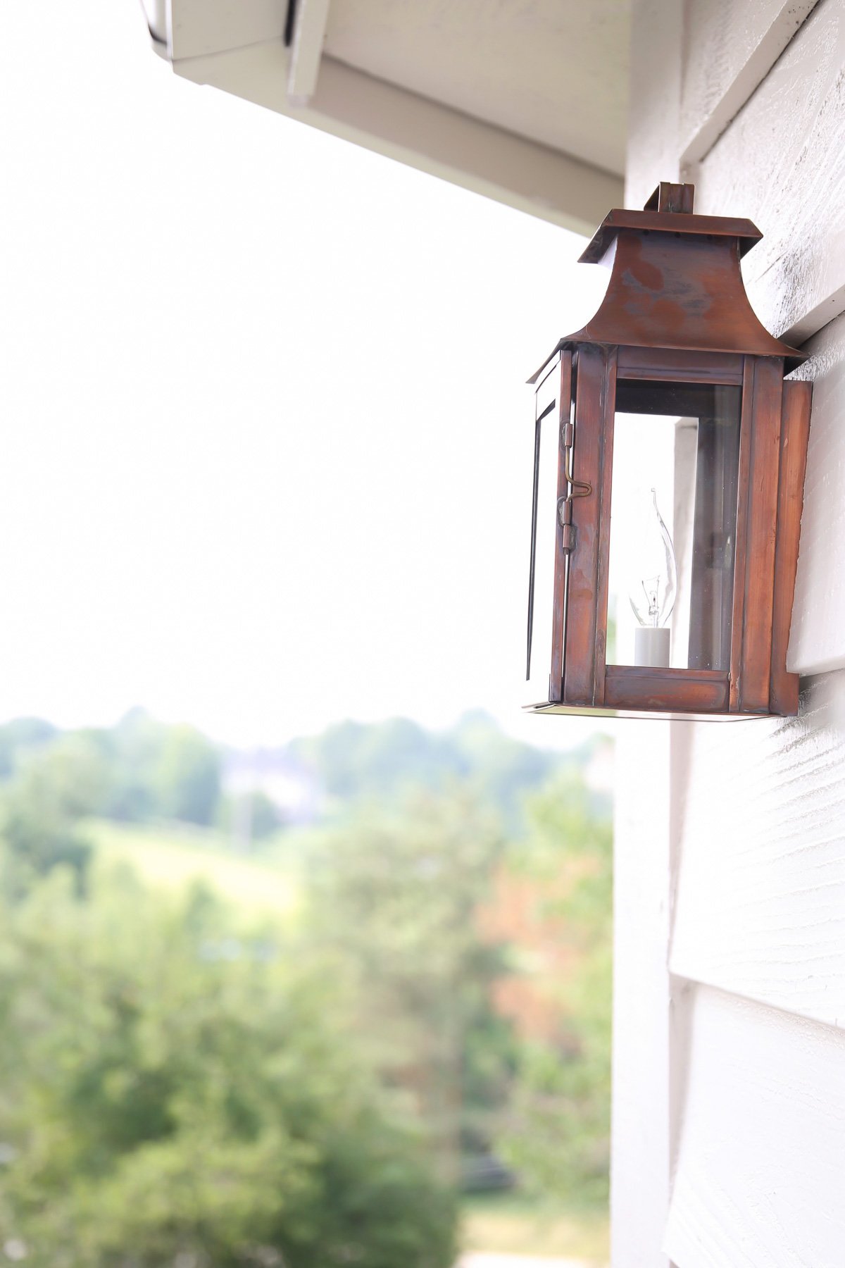 A copper lantern attached to white siding of a home.