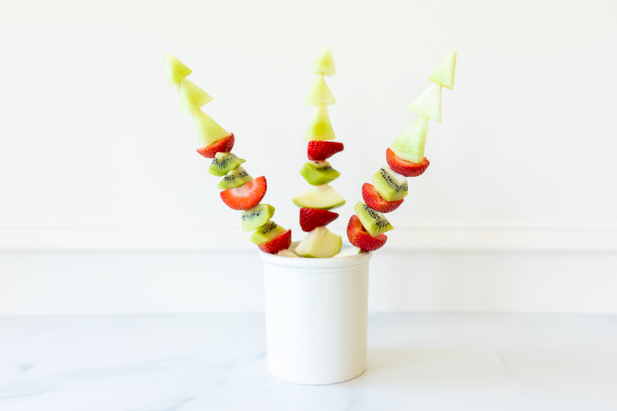 Green and red fruit skewers in a white container.