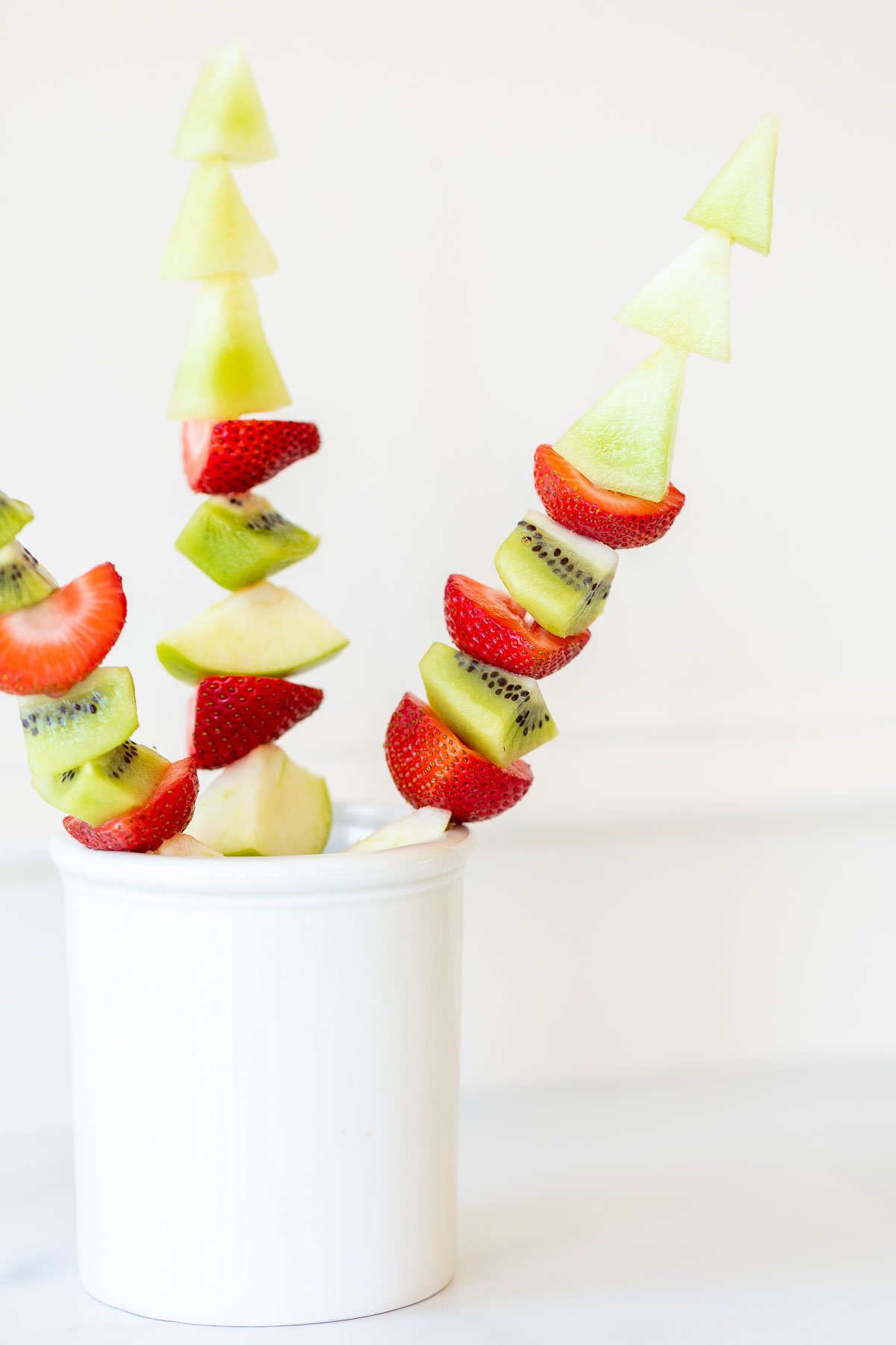 Green and red fruit skewers in a white container.