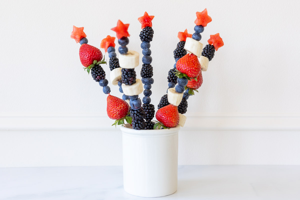 Red white and blue fruit skewers with a star on top in a white jar for display.