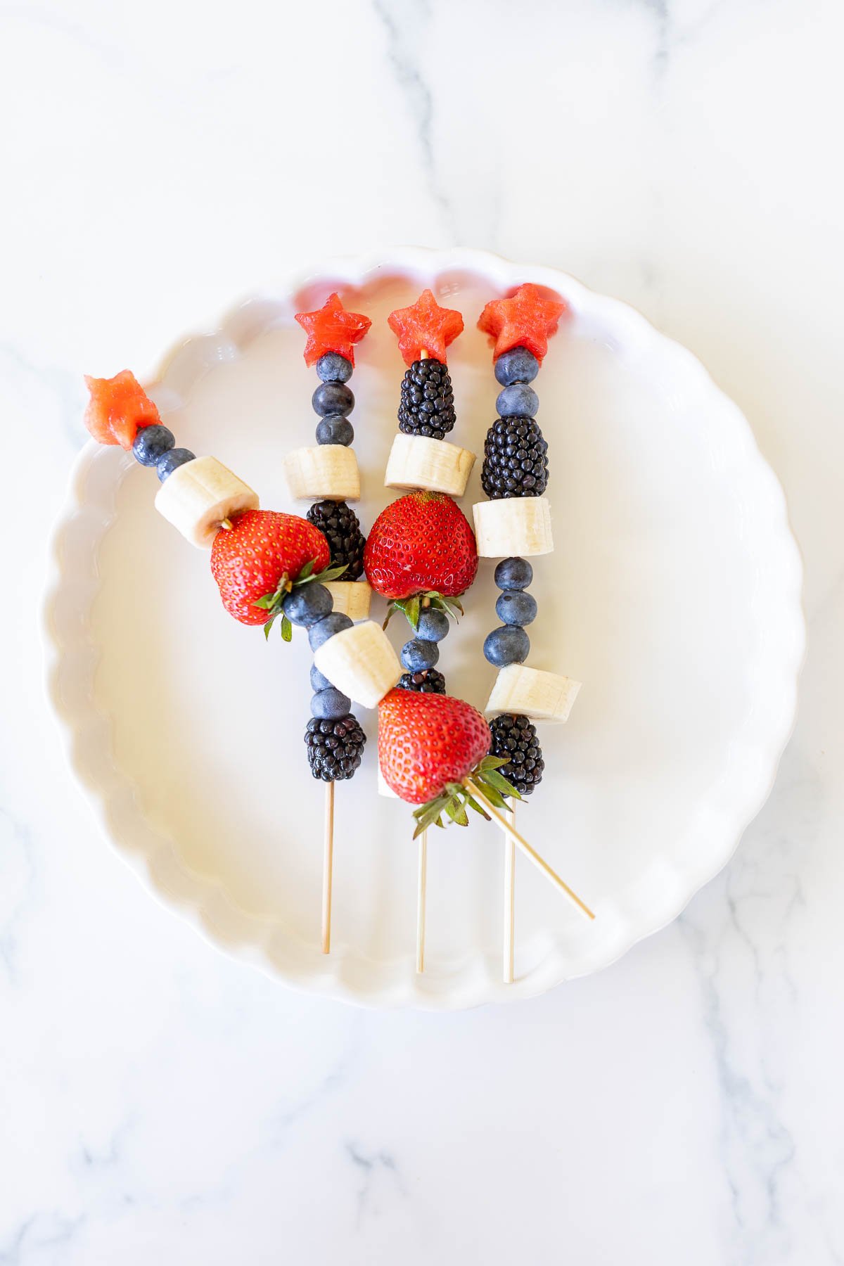 A white plate with red white and blue fruit skewers.