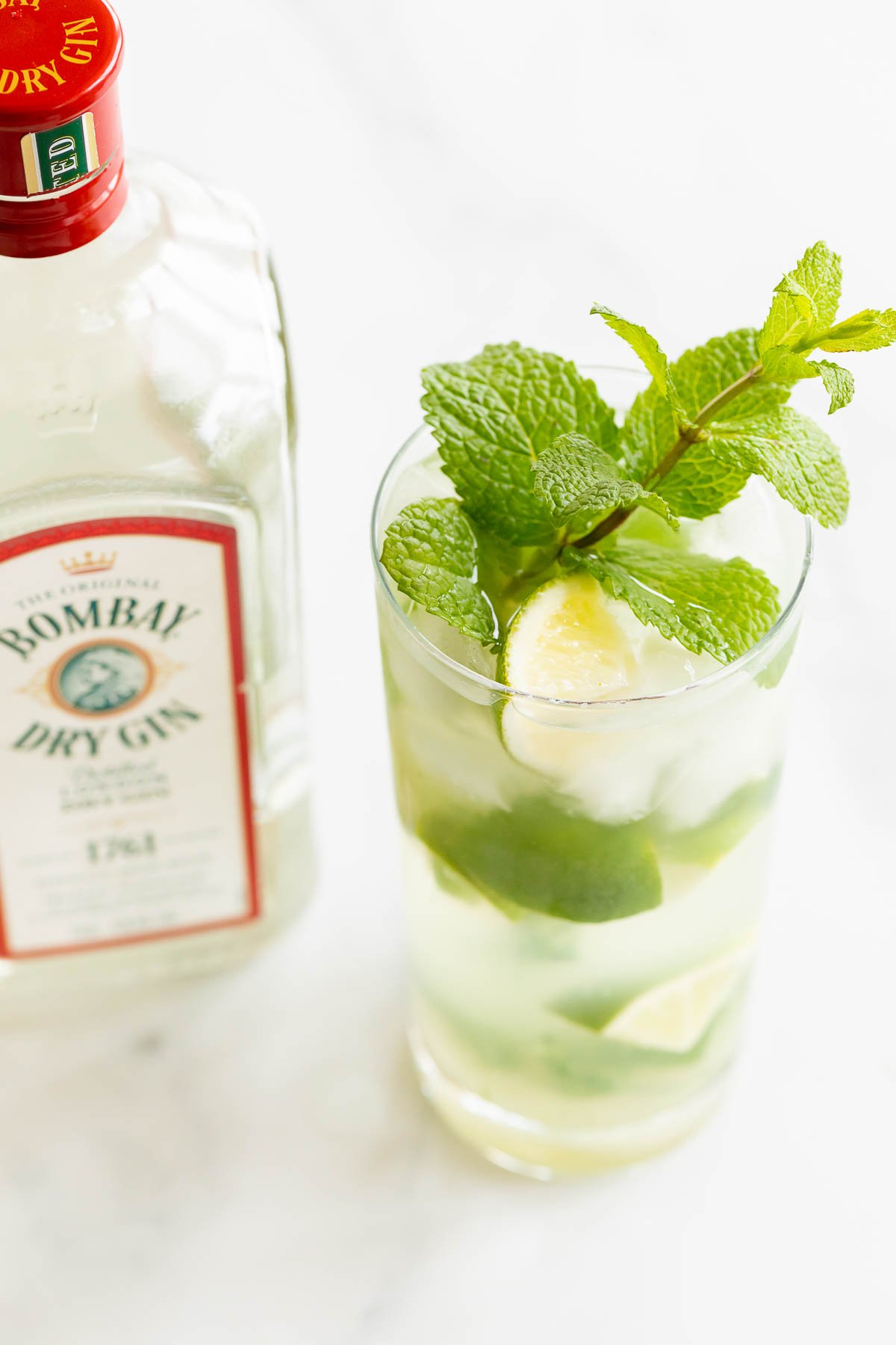 A clear glass full of a gin mojito next to a bottle of Bombay gin.