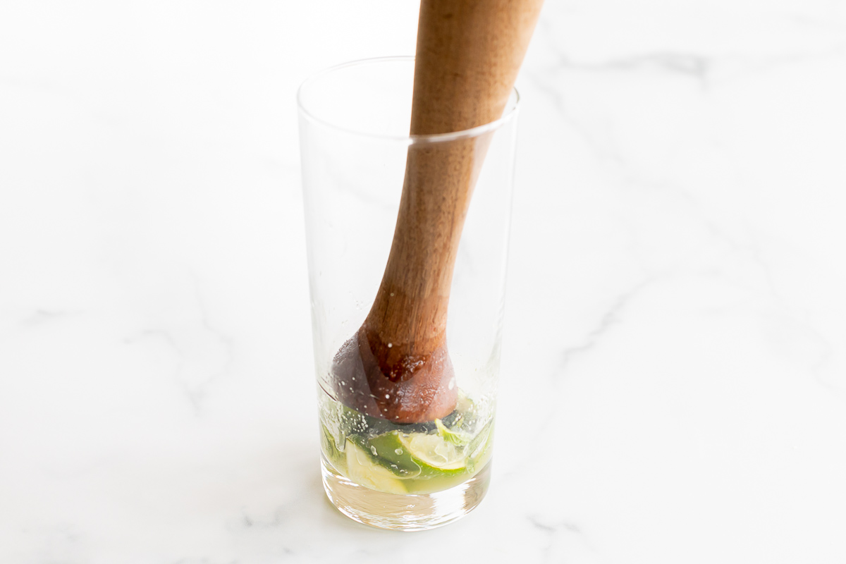 a wooden muddler in a glass full of sliced limes.