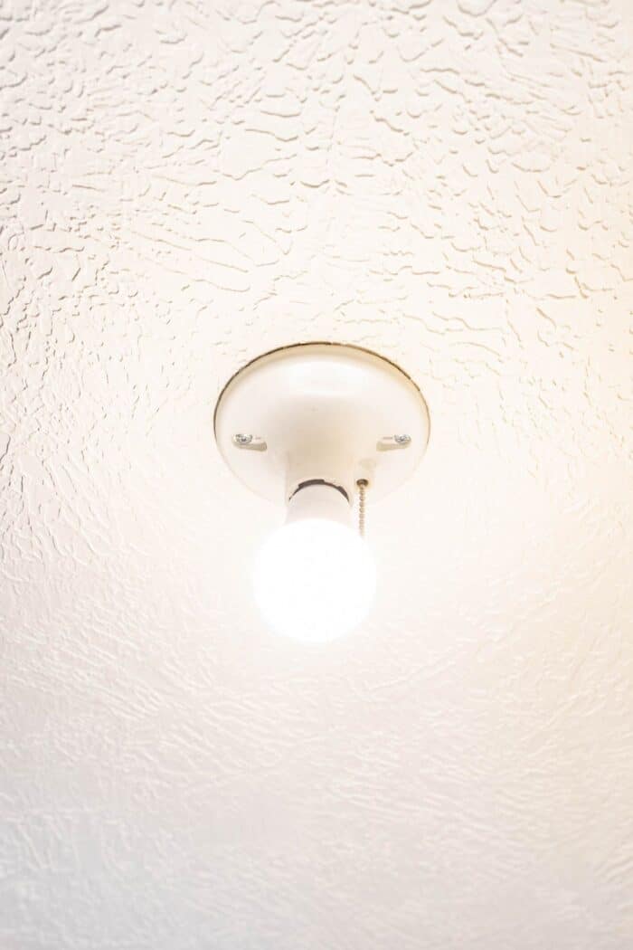 A pull chain light fixture with a bare bulb on a white ceiling.