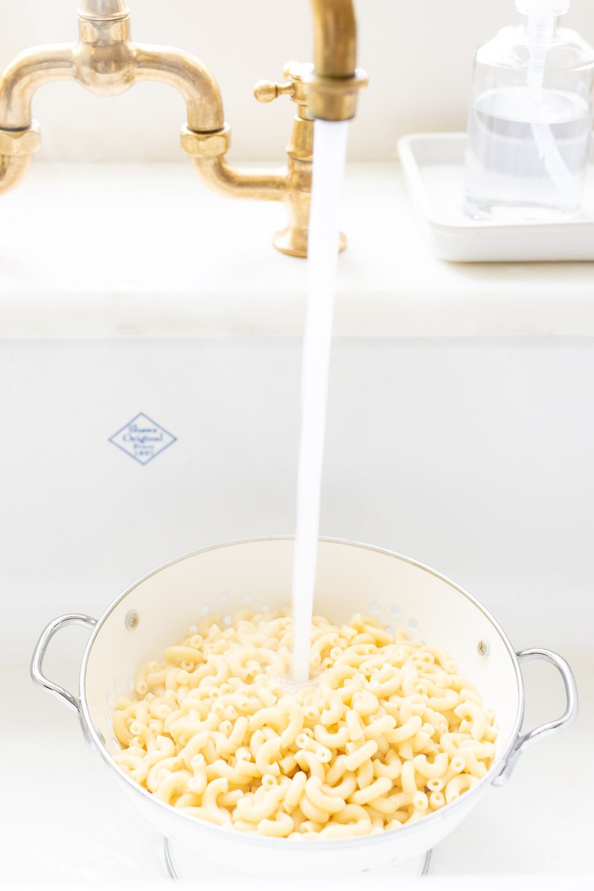 A strainer full of macaroni pasta in a white sink.