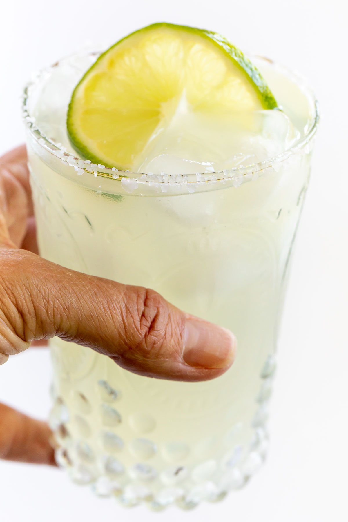 A hand holding a homemade margarita garnished with lime