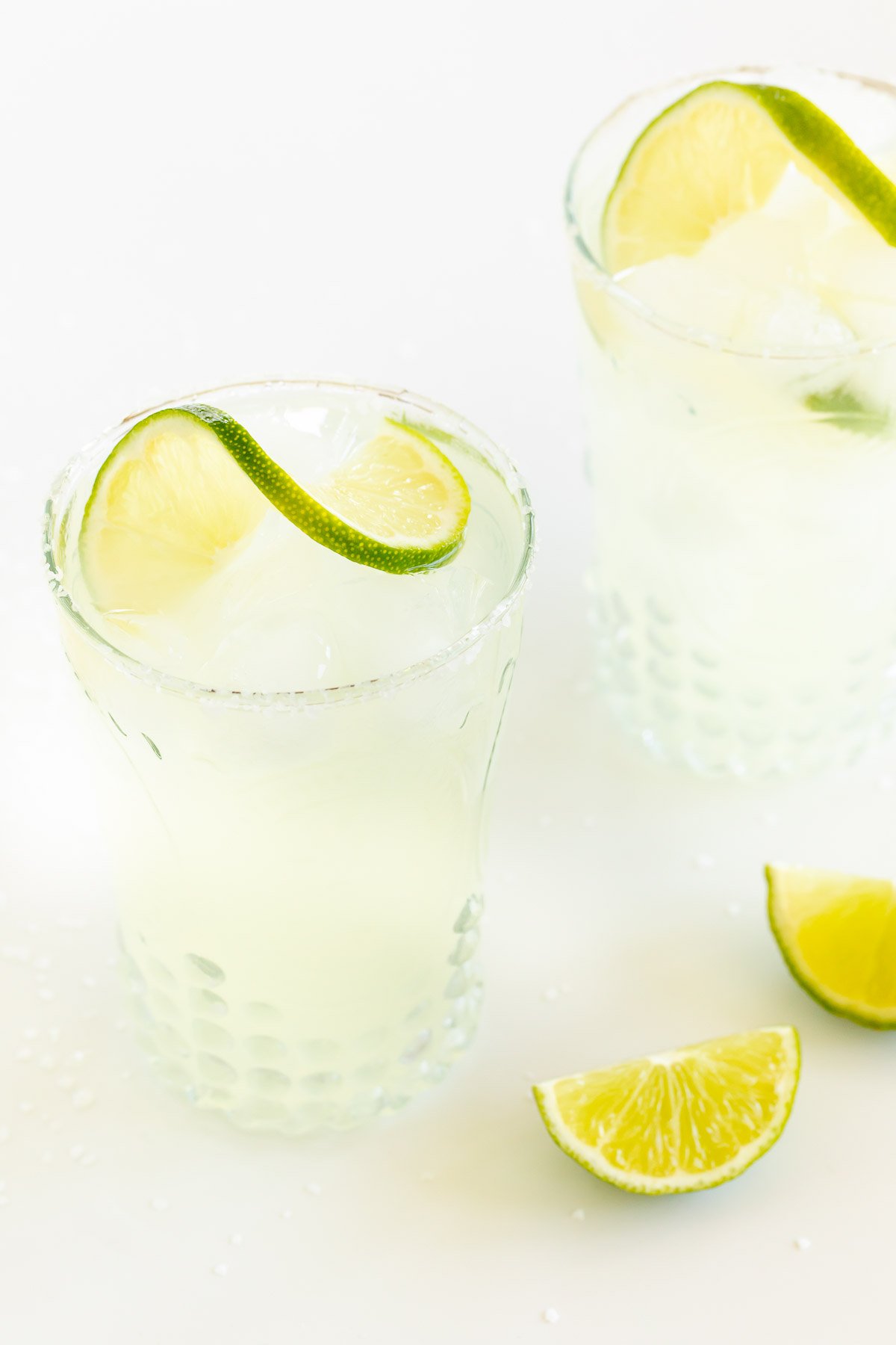 A homemade margarita recipe served up in clear glasses with limes
