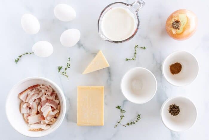 Quiche lorraine recipe ingredients laid out on a marble surface.