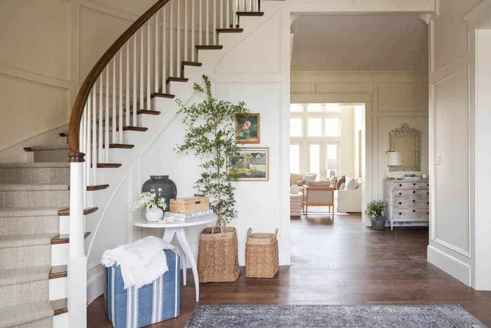 A warm white entryway with a curved staircase, painted in Benjamin Moore Swiss Coffee.