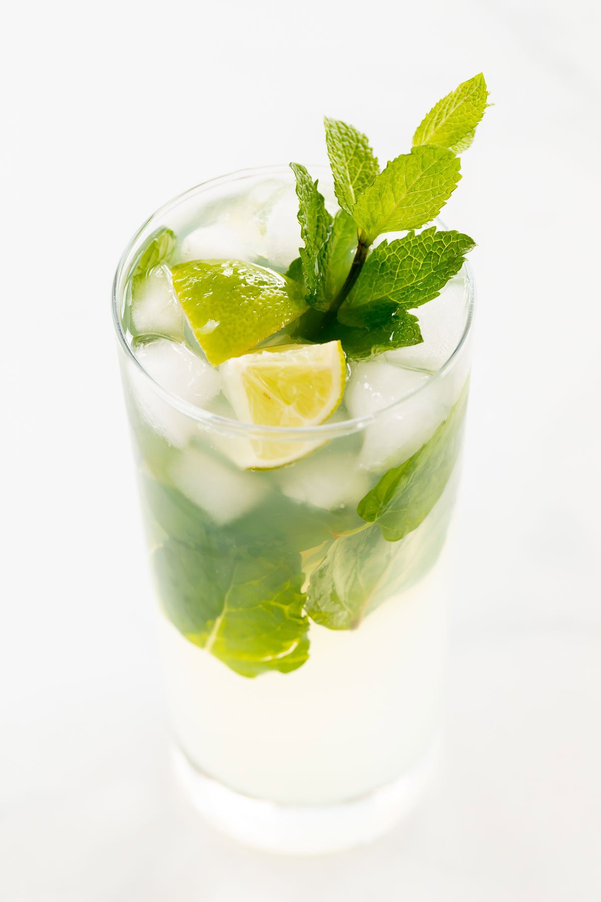 A refreshing tequila mojito cocktail with lime, mint leaves, and ice cubes in a tall glass against a white background.