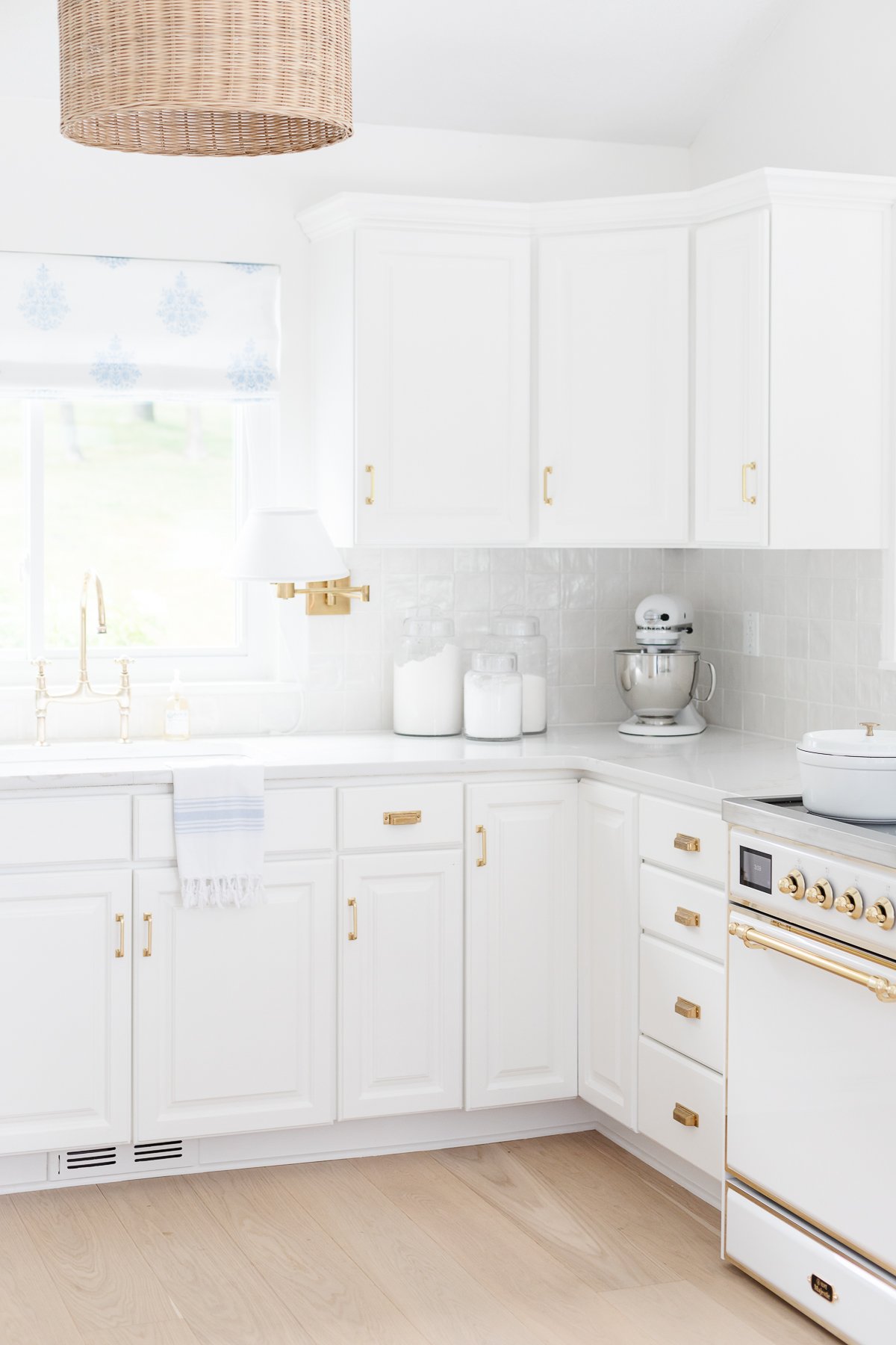 A white kitchen with a brass bridge kitchen faucet over the sink.