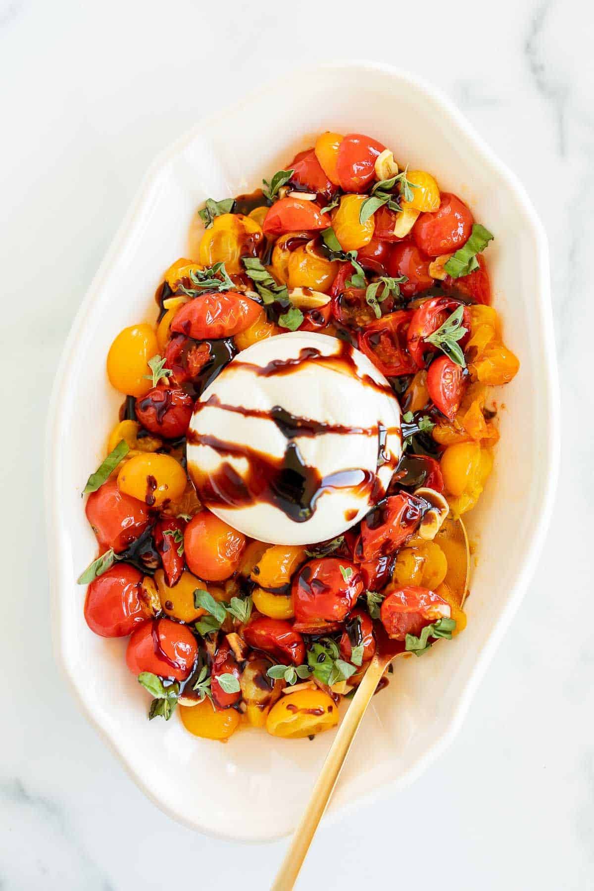 Baked burrata recipe surrounded by roasted cherry tomatoes in a white oval platter.