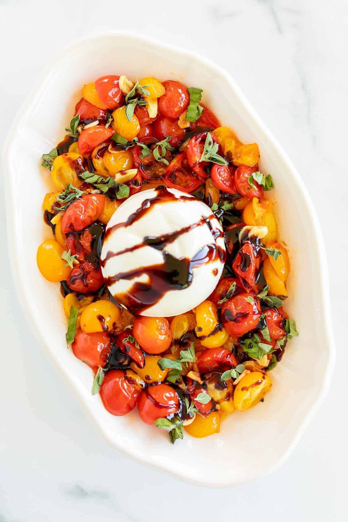 Baked burrata recipe surrounded by roasted cherry tomatoes in a white oval platter.