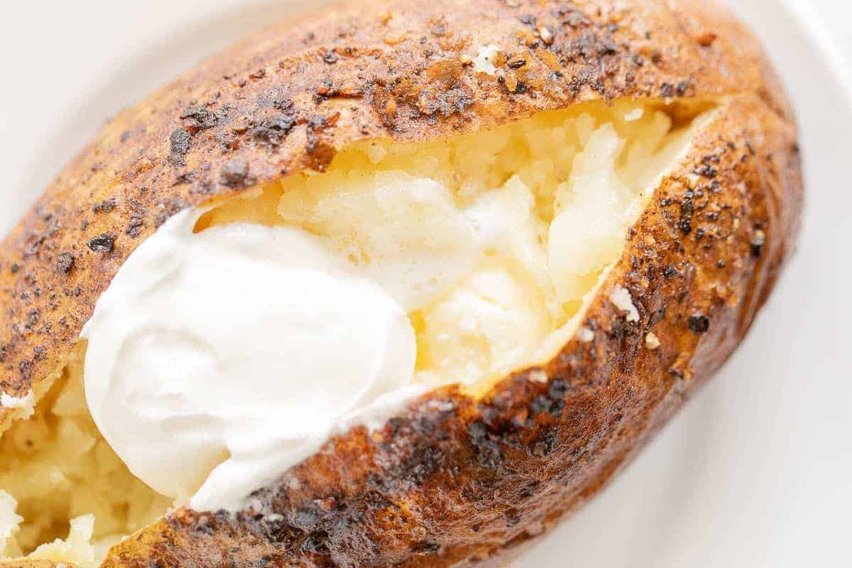 A grilled baked potato sliced open and topped with sour cream.