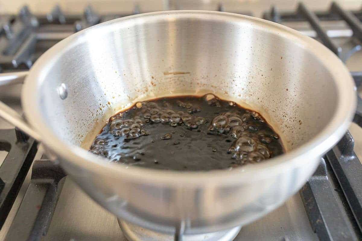 A balsamic vinegar reduction in a silver pan cooking on a stovetop.