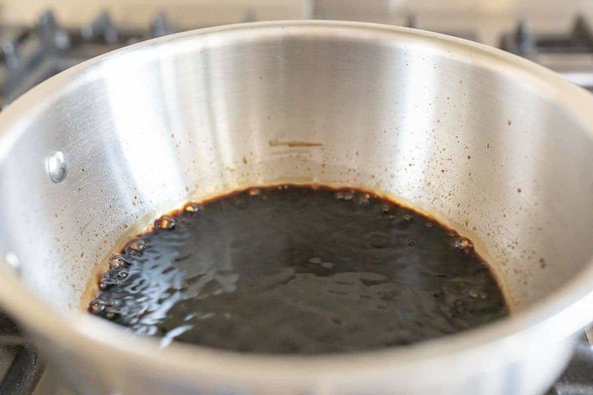 A balsamic reduction in a silver pan cooking on a stovetop.
