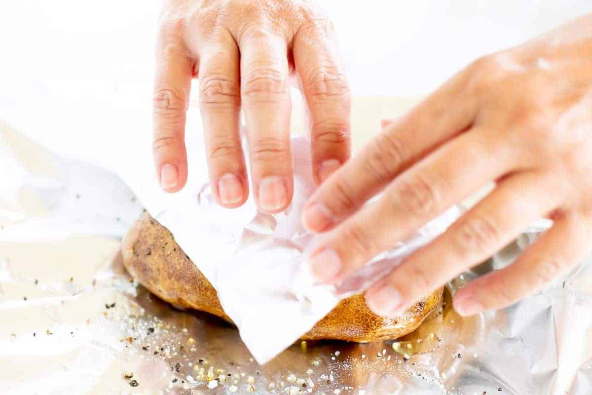 Hands wrapping a grilled baked potato in foil.