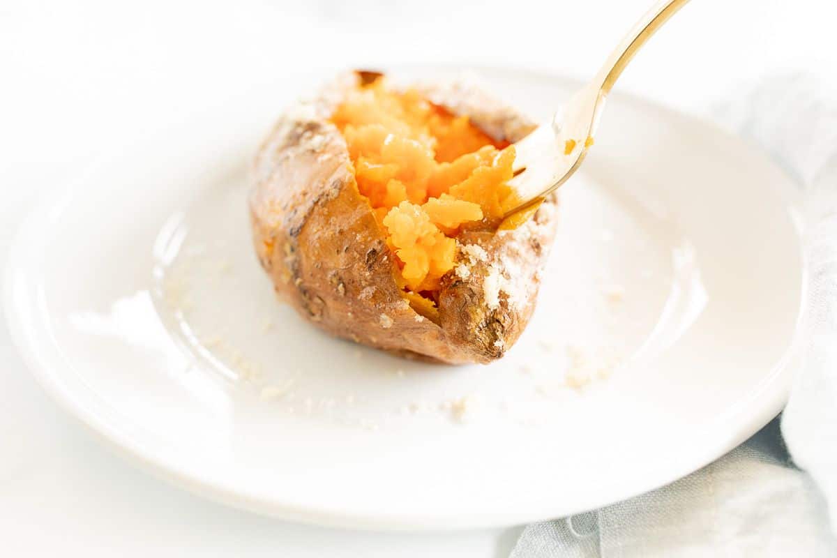 A grilled sweet potato on a white plate, gold fork to the side.