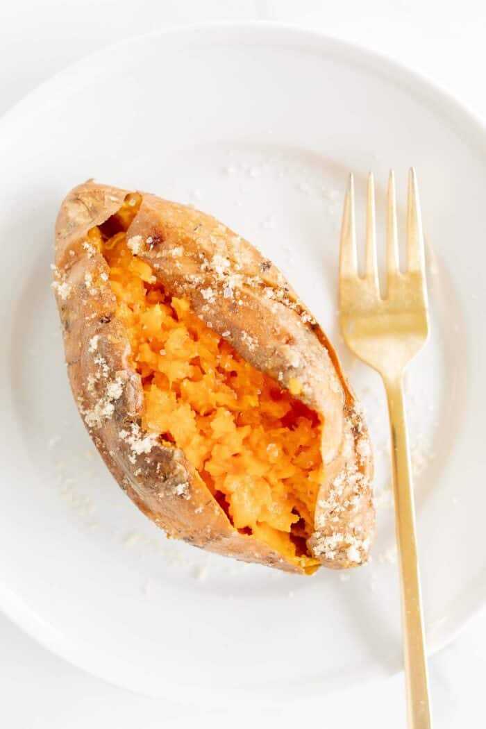 A grilled sweet potato on a white plate, gold fork to the side.