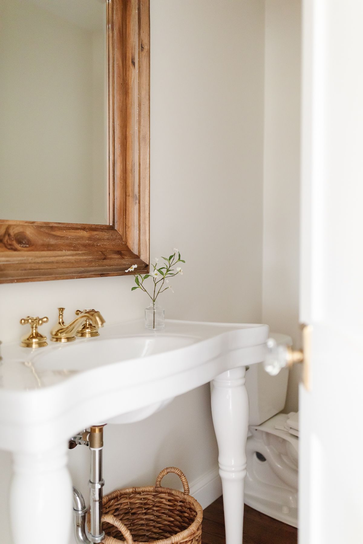 A bathroom with a pedestal sink and wooden mirror
