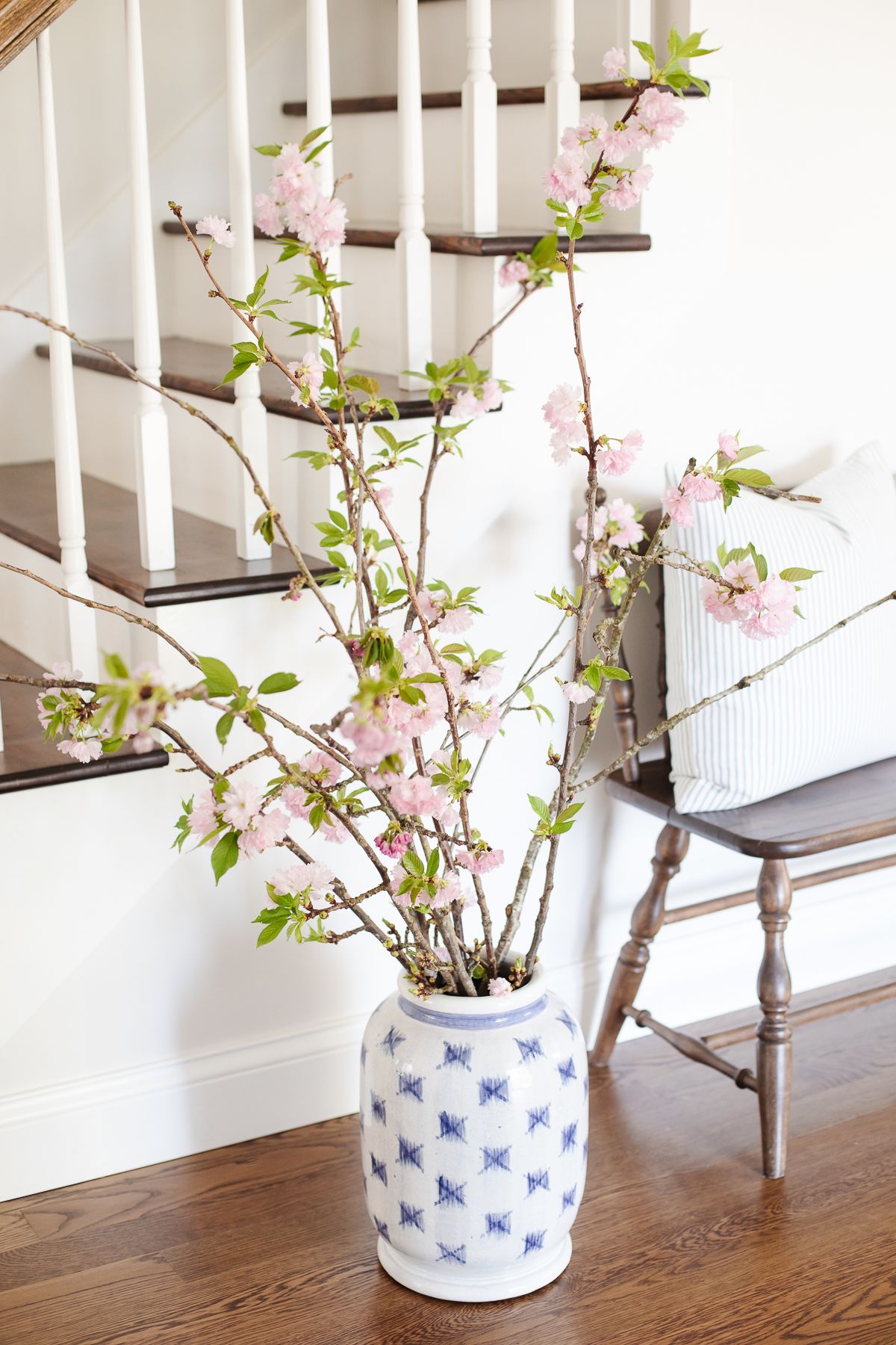 pink blooming branches in a blue and white vase in an entryway, staircase behind