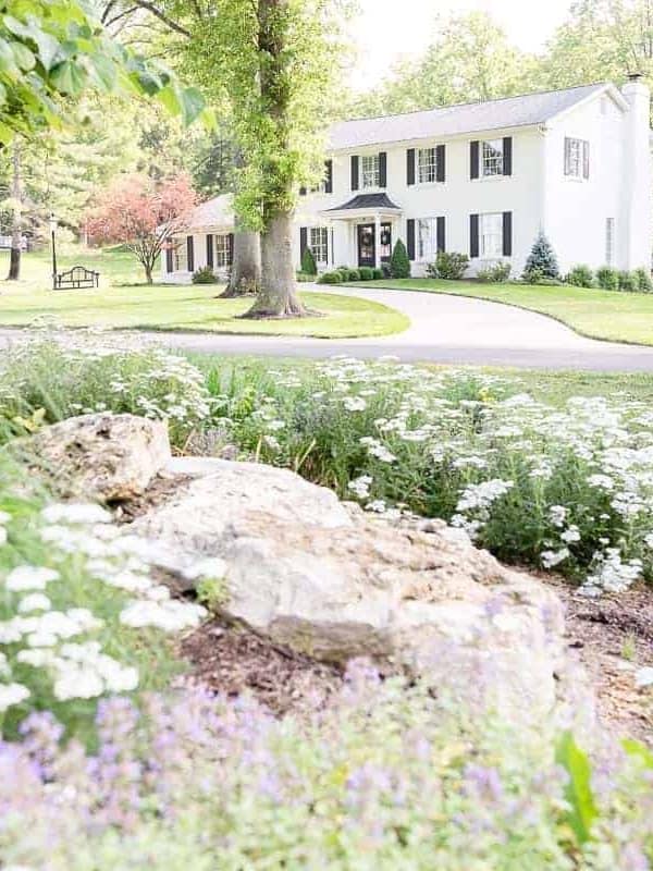 A colonial brick house painted in Benjamin Moore Simply White, flowers in the foreground of image.