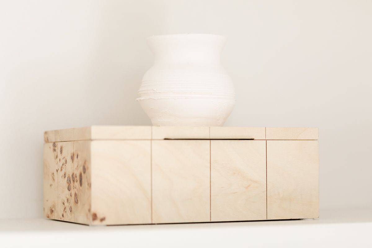 Bookshelf styling of a raw wood box with a small white vase on top.