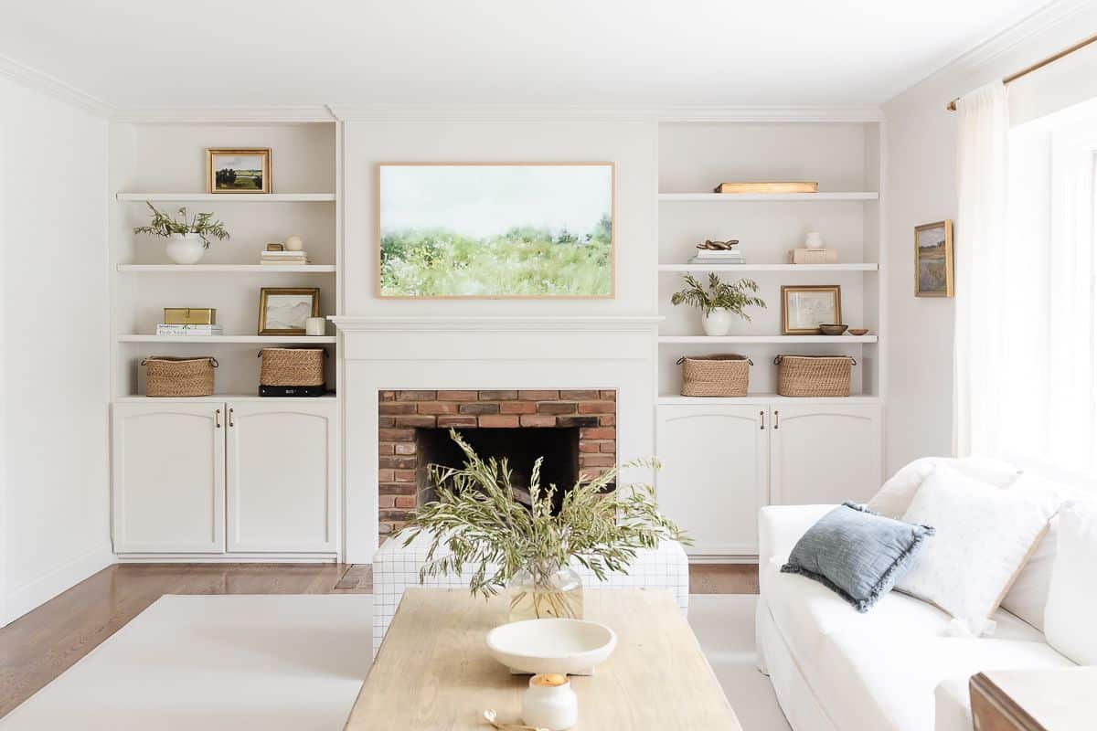 A white living room with bookshelf decor, and a brick fireplace surrounded by built ins,