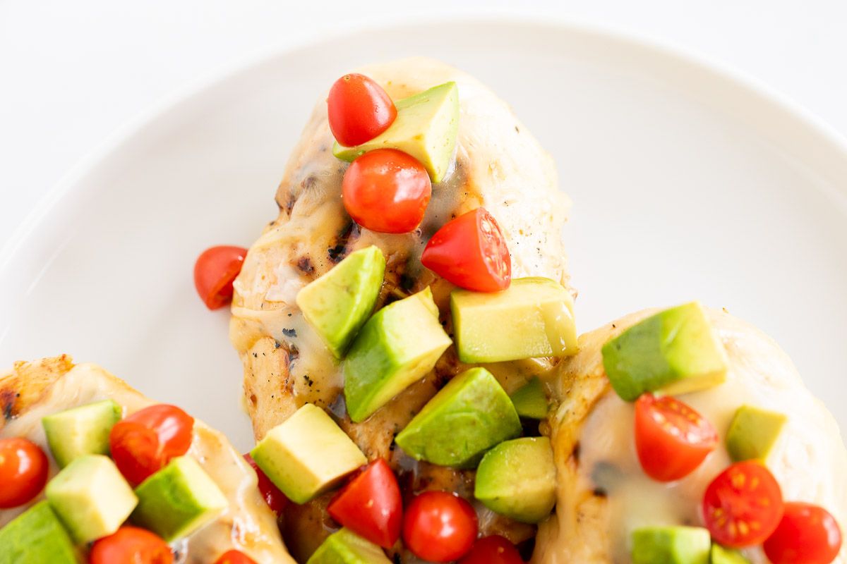 California chicken grill on a white plate, topped with diced avocado and tomato.