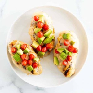 Grilled California chicken on a white plate, topped with diced avocado and tomato.