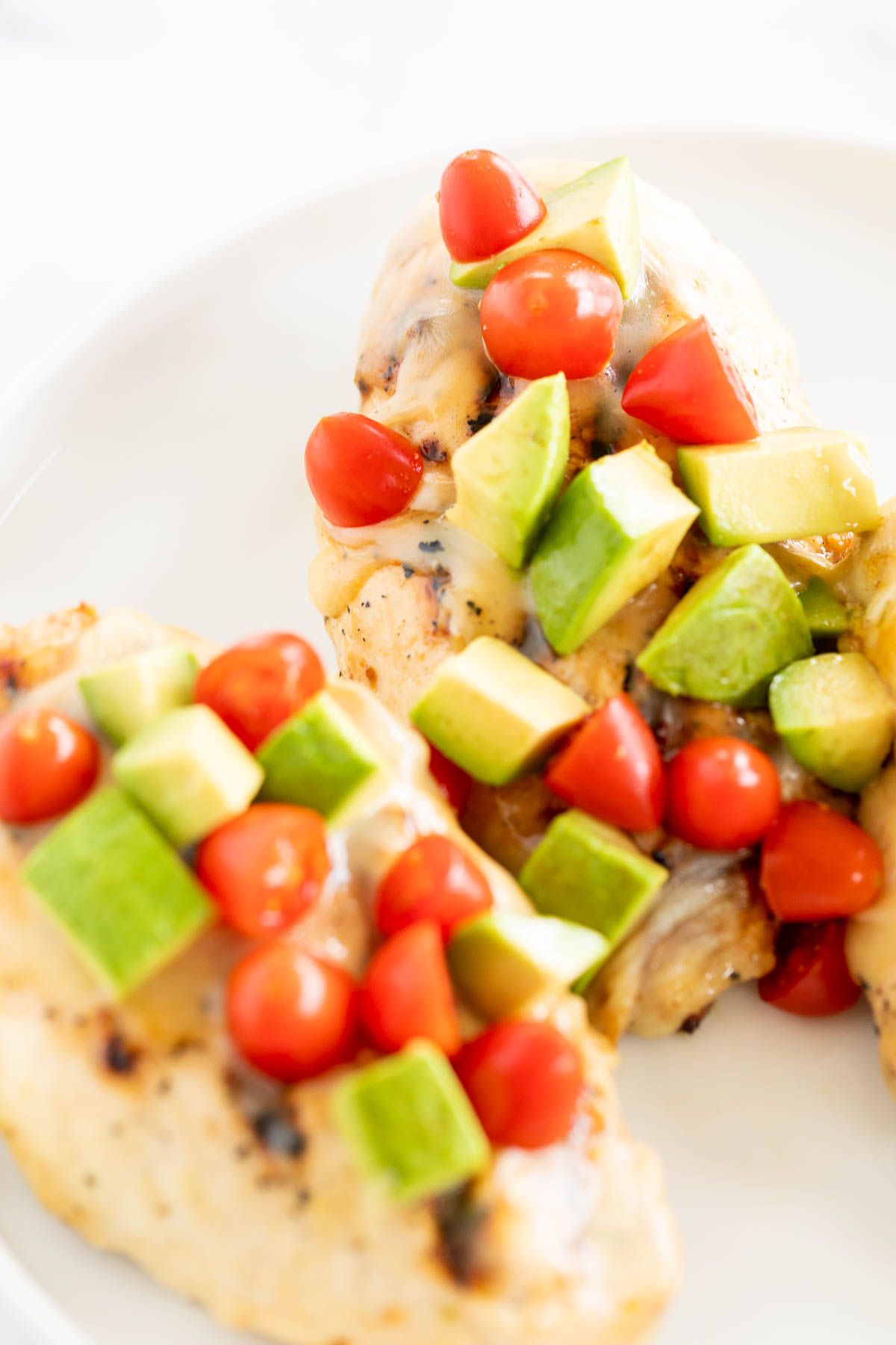 California chicken grill on a white plate, topped with diced avocado and tomato.