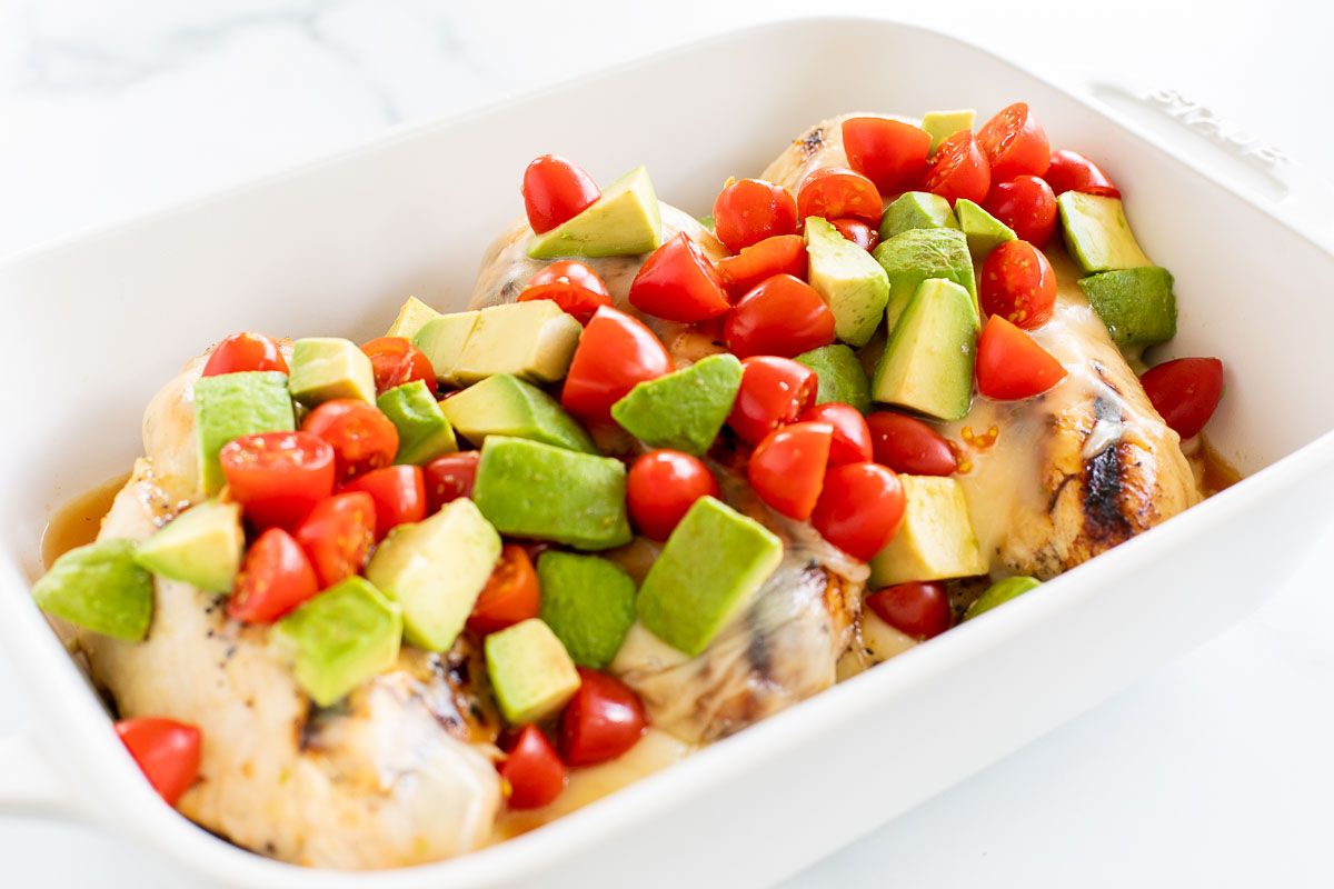 A white baking dish full of california chicken topped with diced tomatoes and avocados.