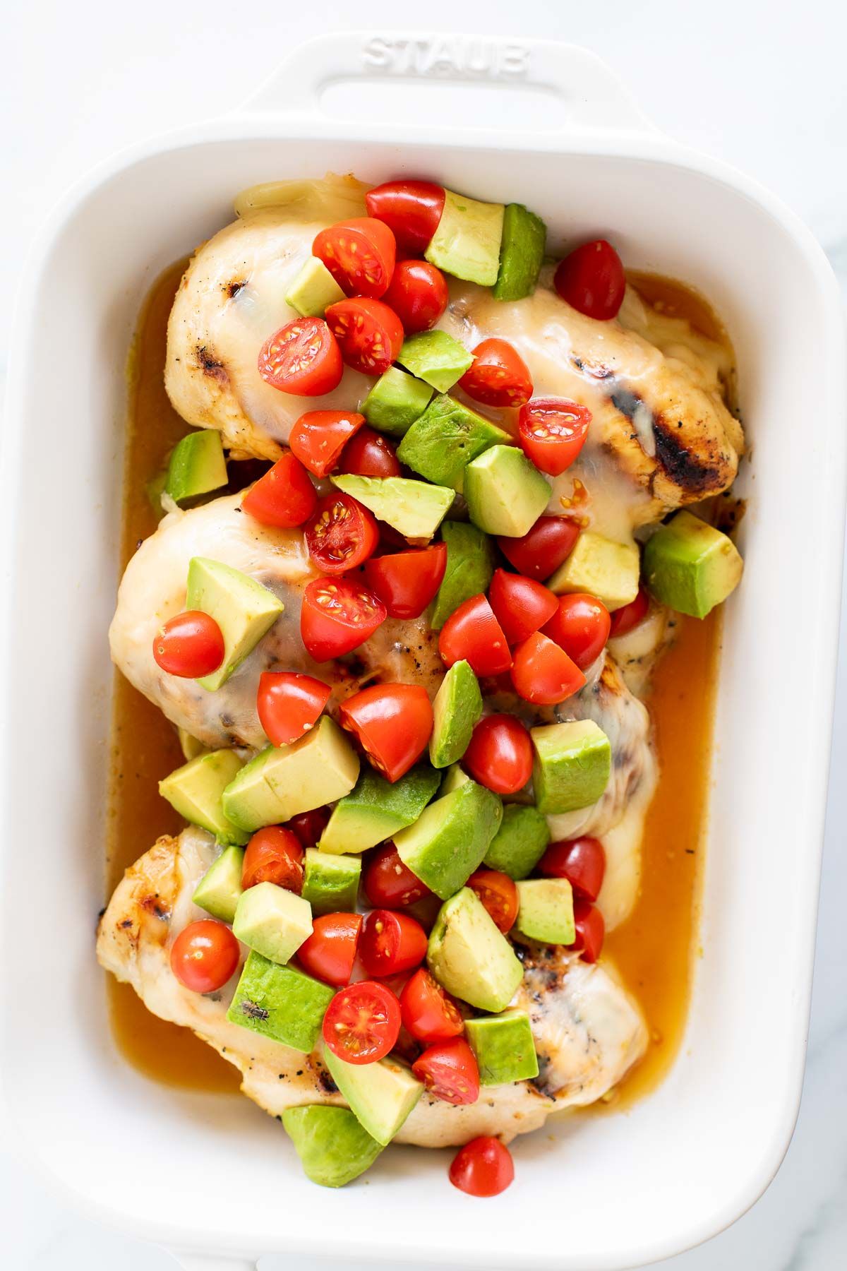 A white baking dish full of california chicken topped with diced tomatoes and avocados.