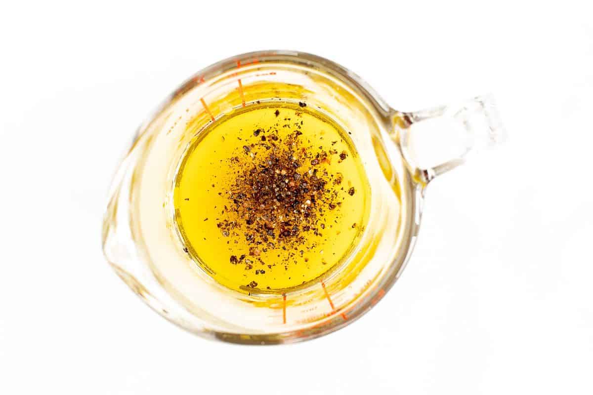 A small glass measuring cup filled with olive oil and seasonings.