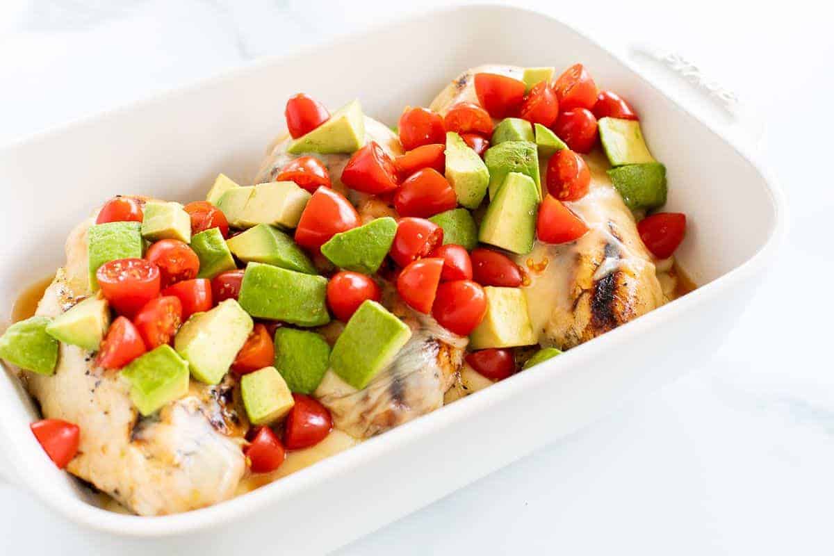A white pan full of California chicken, topped with diced cherry tomatoes and avocado.