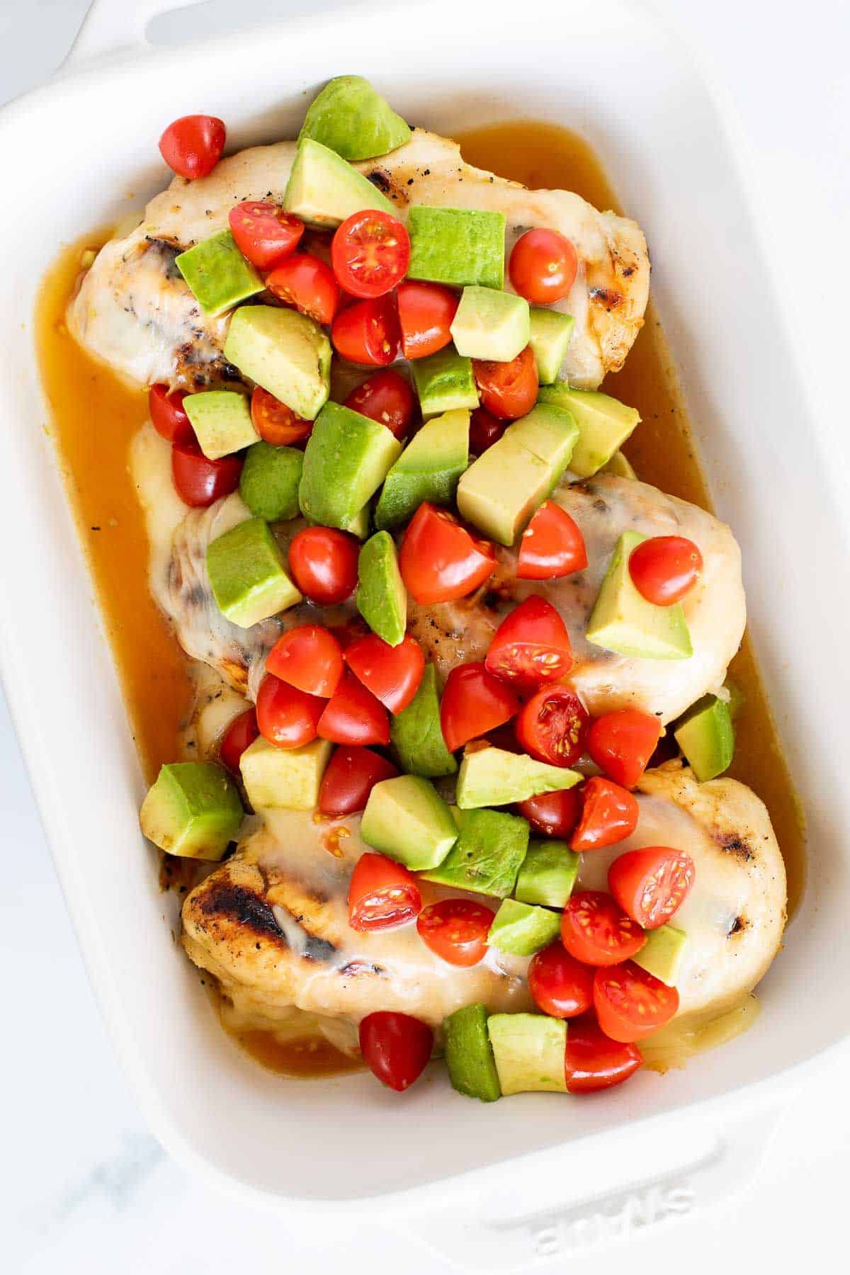A white baking pan filled with California chicken, topped with diced cherry tomatoes and avocado.