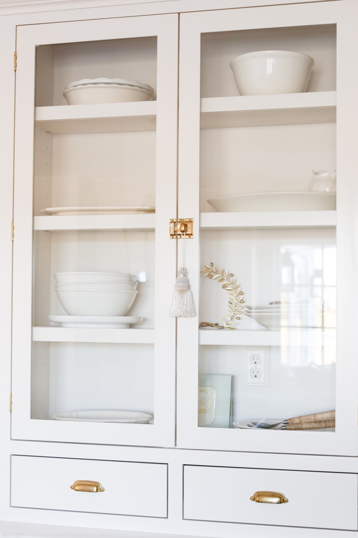 A white hutch with glass doors and custom kitchen cabinets on it.