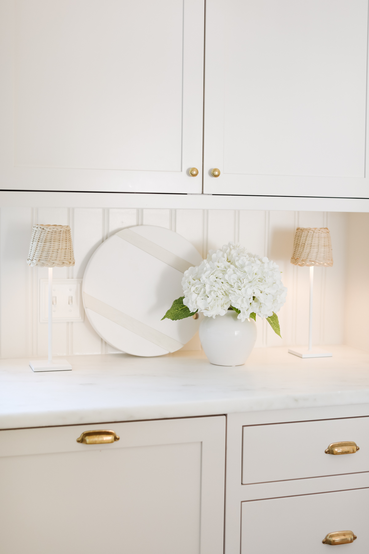 A white kitchen with custom kitchen cabinets and a vase of flowers.