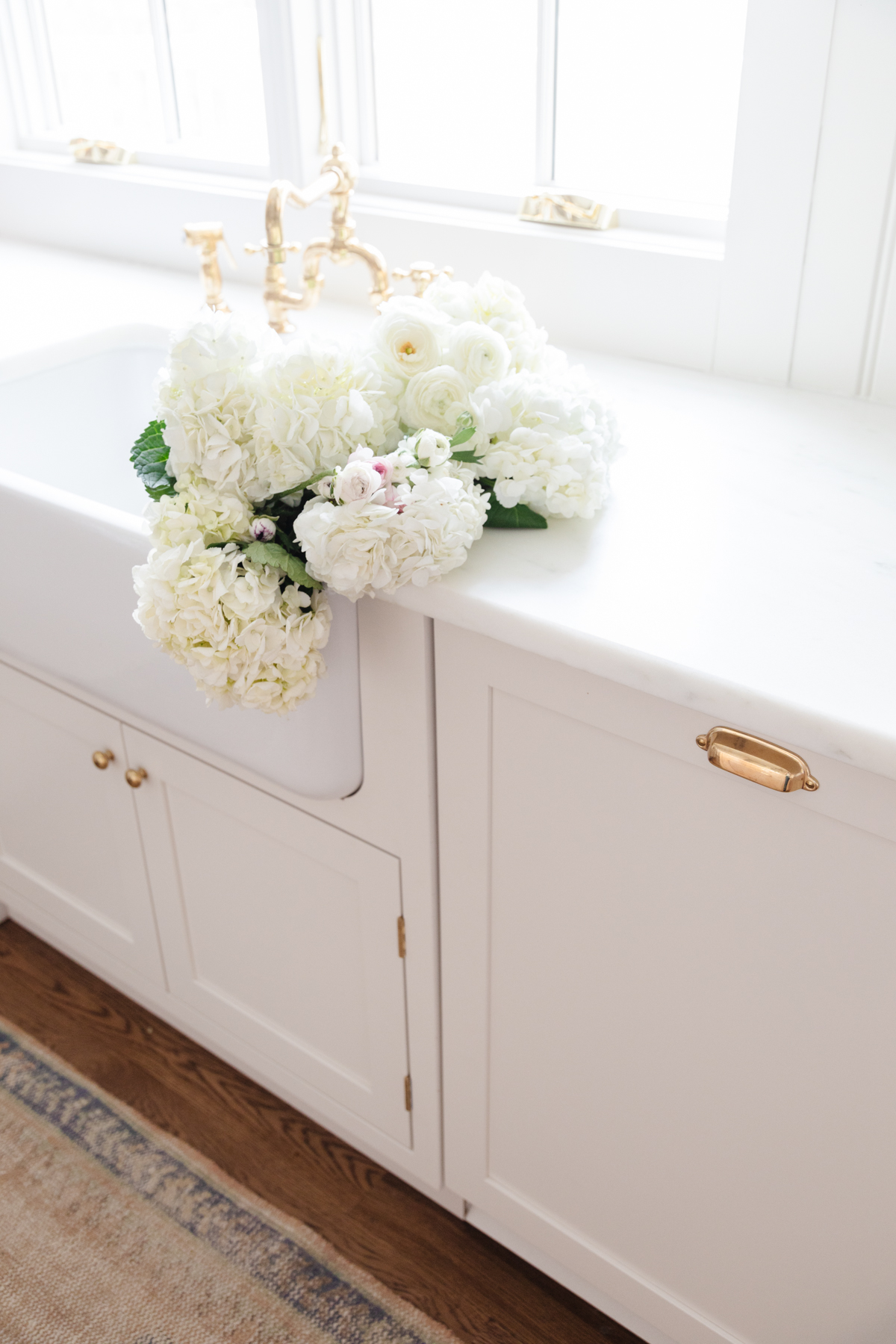 A farmhouse sink with custom cabinetry surrounding, and white flowers inside. 