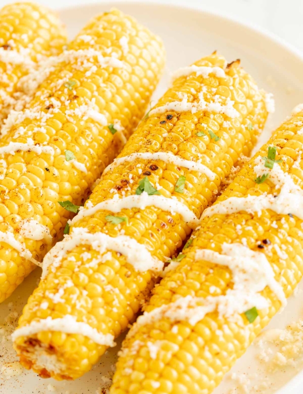 Elote (Mexican corn on the cob) drizzled with crema on a white plate.